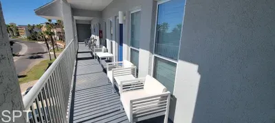 Spacious coastal walkway with seating, bright views, and palm‑lined surroundings — a relaxing outdoor corridor offering fresh air and easy access to each unit.