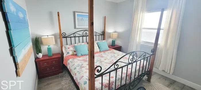 Bright and inviting primary bedroom featuring a wrought‑iron canopy bed, floral linens, turquoise accents, and abundant natural light — a relaxing retreat designed for comfort and style.