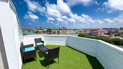 Rooftop patio with turf flooring, cozy wicker seating, and turquoise cushions. Enjoy open‑sky relaxation with scenic coastal views—perfect for morning coffee or sunset lounging.