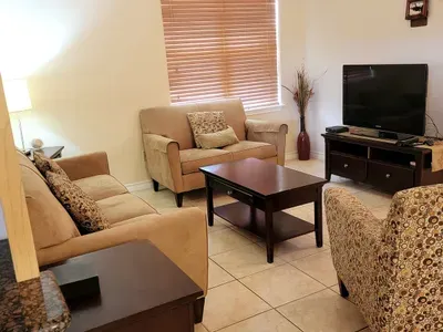 Settle into this cozy living room featuring comfortable seating, warm tones, and a neatly arranged layout. With tiled floors, soft lighting, and a well‑placed TV, it offers an inviting space for relaxing, gathering, and unwinding during your stay.