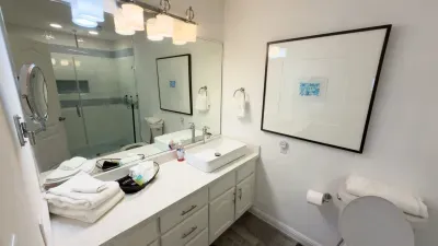 Sleek Spa-Like Bathroom Oasis
Refresh in elegance: crisp white vanity with vessel sink, fluffy towels, and amenities ready. Framed abstract art glows under pendant lights; glass shower with subway tiles beckons. Wood floors and toilet complete this.