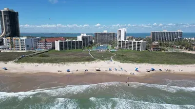Beachfront resort setting with wide sandy shores, gentle waves, grassy dunes & multi‑story ocean‑facing buildings. Umbrellas, pathways & open coastal views create a relaxing, guest‑ready environment perfect for enjoying sun, sand & shoreline comfort.