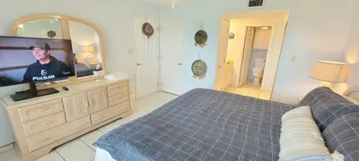 Cozy, well‑kept bedroom featuring a plush serene bed with layered pillows, a spacious dresser with mirror, soft lighting, and direct access to the bathroom. Clean décor, organized storage, and a calm, inviting layout create an easy, restful stay.