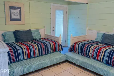 Cozy twin bedroom with trundles, bright coastal décor, and space‑saving layout—perfect for kids or groups. Light pastel walls, striped bedding, and private patio access create a cheerful, beach‑ready retreat.