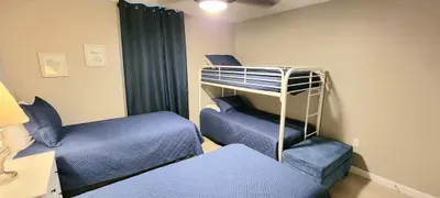 Bright, family‑friendly bedroom featuring twin beds and a cozy bunk setup, unified with soft blue bedding, warm lighting, and simple décor. Ideal for groups seeking comfort, space efficiency, and a relaxed retreat near the coast.