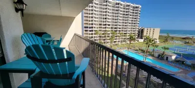 Relaxing balcony retreat with turquoise seating overlooking the pool, palms, tennis courts, and sparkling coastline. A perfect spot to unwind, enjoy morning coffee or sunset breezes, and take in sweeping resort and ocean views throughout your stay.