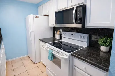 A compact, coastal‑bright kitchen where simplicity meets comfort — crisp white cabinetry, dark granite contrast, and soft blue walls create a clean, inviting vibe perfect for easy mornings and relaxed evenings in your South Padre getaway.