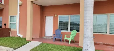 Inviting ground‑level entry with a clean patio, colorful seating, and easy access to the unit. Bright exterior, simple outdoor setup, and nearby greenery create a welcoming spot to relax before heading inside to enjoy your stay.