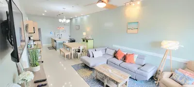 Bright, open living and dining space featuring a cozy sectional, warm accents, and a modern kitchen backdrop. Soft green walls, natural light, and inviting décor create a comfortable, welcoming area perfect for relaxing and gathering.