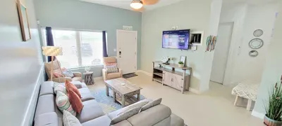 Spacious, light‑filled living and dining area featuring a cozy sectional, warm textures, and a modern kitchen backdrop. Soft green walls, natural light, and inviting décor create a comfortable, open space ideal for relaxing and gathering.