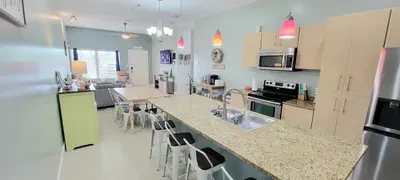 Bright open‑concept kitchen and dining area featuring light wood cabinetry, stainless appliances, and a spacious granite island with bar seating. Warm lighting, modern décor, and a connected living space create an inviting, comfortable layout.