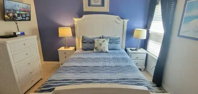 Relax in this bright coastal bedroom featuring a plush serene bed, crisp striped linens, soft lighting, and calming blue accents. Enjoy a peaceful retreat with ample storage, blackout curtains  beach‑inspired atmosphere perfect for unwinding.