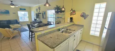 Enjoy a bright open‑concept space featuring a granite kitchen, pendant lighting, cozy seating, and large windows that fill the room with natural light. Thoughtful décor, dining space, and a warm coastal vibe create a welcoming area for relaxing.