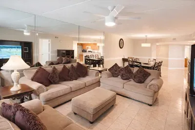 Spacious coastal retreat with open-concept living, plush seating, mirrored wall, and full kitchen—perfect for relaxing or entertaining near the beach.