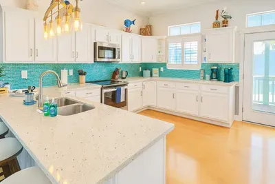 Cook and gather in this stunning coastal kitchen featuring gleaming quartz countertops, bright white cabinetry and sea glass tile backsplash. Enjoy modern appliances, stylish lighting & a spacious breakfast bar—perfect for group meals & entertaining.