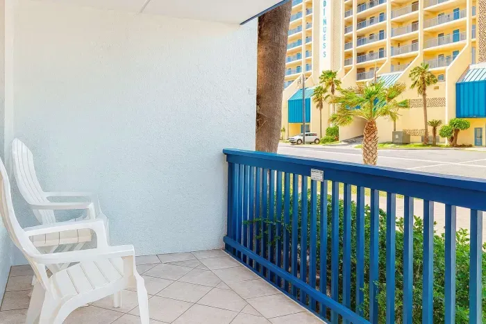 Serene White Balcony
Adirondack Chairs Over Palm-Lined Complex. Crisp stucco terrace w/ blue railings & 2 comfy white chairs overlooks swaying palms, parked cars & beige high-rise. Breezy spot for sunset cocktails & people-watching in coastal haven!