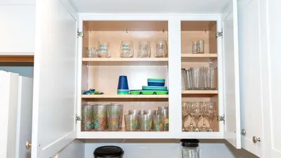 Ample Kitchen Cabinets:
Glasses, Mugs & Tupperware Ready. Spacious white uppers stocked w/ colorful tumblers, wine glasses, blue storage & patterned mugs beside fridge. Everything for beach picnics & sunset toasts—fully equipped for fun!