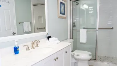 Fresh Coastal Bath
Glass Shower w/ Marble Vanity. Light teal haven boasts frameless shower, crisp subway tile, marble-top double vanity & plush towel stacks. Seashell frame & amenities delight—refresh in luxury before beach days!