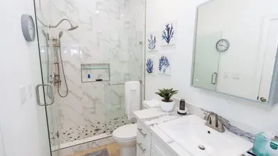 Stylish bathroom featuring a polished marble countertop, modern fixtures, and a spacious vanity with organized storage. Bright lighting and a seamless connection to the laundry area create a fresh, functional space ideal for extended or short stays.