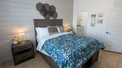 Serene bedroom retreat featuring a cozy wooden bed with crisp white linens, blue floral comforter, and warm ambient lighting. Thoughtful décor, framed art, and soft textures create a tranquil, inviting space perfect for restful nights.