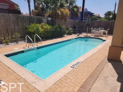 Relax by the sunlit outdoor pool surrounded by loungers, umbrellas, and a long fenced deck—an inviting retreat perfect for unwinding, enjoying warm afternoons, and creating a peaceful escape just steps from your stay.