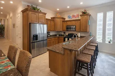 Modern kitchen with granite counters, stainless steel appliances, woven barstools, and vibrant decor. Bright, spacious layout ideal for cooking, entertaining, and relaxing. Natural light and stylish touches throughout.