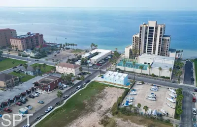 A bright coastal setting with an open, easygoing feel, where the shoreline and surrounding buildings create a calm sense of place. The steady ocean backdrop brings a relaxed rhythm, offering a naturally inviting starting point for an unhurried stay.