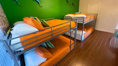 Fun and vibrant bunk room featuring two sets of sturdy metal bunks, bright orange bedding, and tropical pillows—ideal for kids or groups looking for a playful, comfortable, and spacious place to unwind after beach adventures.