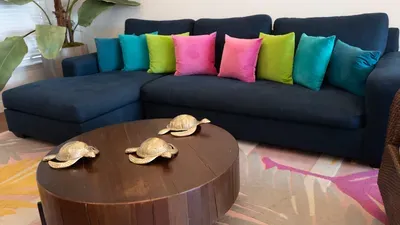 Stylish sectional sofa in deep blue, with vibrant pillows and tropical plants nearby, creates a lively, relaxing gathering space. Unique sea turtle decor adds a fun coastal touch, perfect for vacation lounging.