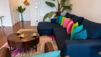Spacious sectional sofa with vibrant pillows, lush plants, and a stylish coffee table create a lively and comfortable living area—perfect for relaxing after a day in the sun or gathering with friends and family.