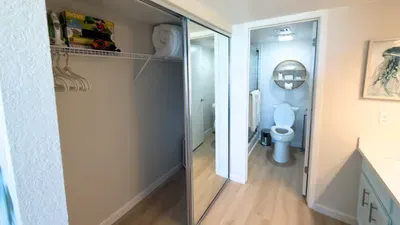 Bright hallway with mirrored closet leading into a clean, modern bathroom featuring white tile, a round mirror, and organized storage, offering guests a tidy, efficient space designed for smooth routines and a comfortable, well‑kept stay.