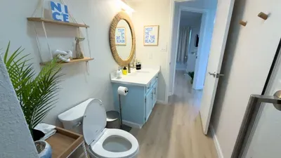 Fresh, thoughtfully designed bathroom featuring a blue vanity with woven‑frame mirror, glass shower, and soft neutral finishes, giving guests a clean, calming space ideal for easy routines, refreshing mornings, and a well‑kept, spa‑inspired feel.