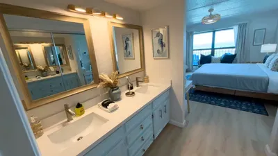 Spacious, well‑lit bathroom featuring a double‑sink vanity with gold‑framed mirrors, warm lighting, and a private toilet area, giving guests a clean, organized space designed for smooth routines, comfortable mornings, and an elevated stay experience.