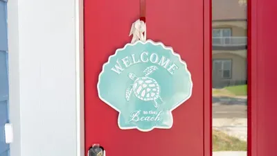 Welcoming Turtle Shell Door
Charming red door w/ seashell turtle "Welcome to the Beach" sign! Views to blue home & sunny SPI street at 114 Pike St Unit A. Invites you to direct beach access paradise. Enter the fun!
