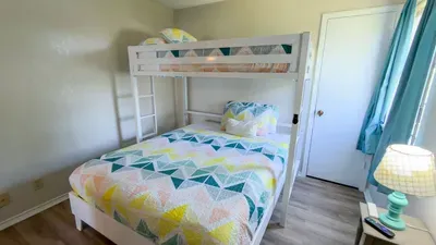 Fun Bunk Bed Kids' Paradise
Cheerful bunk room for little adventurers in South Padre! White twin-over-full bunk w/ vibrant triangle quilt matching master. Soft lamp, blue drapes, wood floors. Ideal family sleep near beach & SpaceX thrills!
