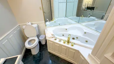 Luxurious Jetted Tub Spa Bathroom
Elegant en-suite bath in South Padre retreat! Deep jetted soaking tub w/ gold fixtures, crisp white toilet, plush towels. Mirrored vanity, wainscoting, dark tile floors. Unwind in luxury post-beach.