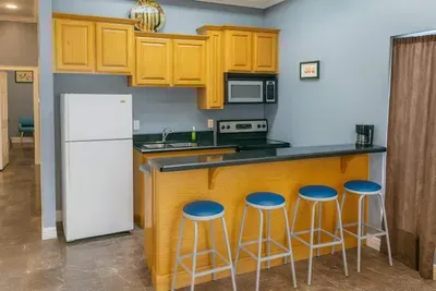 Cozy Breakfast Bar Kitchen
Whip up meals in the fully stocked kitchen with wood cabinets, white fridge, stove, microwave, double sink, and black granite counters. Four blue barstools create a casual breakfast bar hangout.