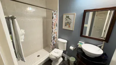 Charming Floral Shower Haven
Lather up in the walk-in shower with patterned curtain, pedestal sink on wood vanity, wood-framed mirror, and plant art. Towels, soap, and toiletries await in this blue-accented guest bath.