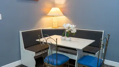 Elegant Corner Dining Nook
Gather around the white farmhouse table with blue-cushioned metal chairs in the cozy booth seating. White orchids and a shell lamp brighten this perfect spot for beachside meals.