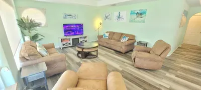 Spacious coastal living room with plush recliners, beach‑themed art, warm lighting, and a relaxed, family‑friendly vibe—perfect for unwinding after sun‑soaked days on the island.