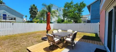 Sunny fenced‑in backyard with outdoor dining set, umbrella shade, and a relaxed coastal vibe—perfect for enjoying meals, morning coffee, and easy island downtime.
