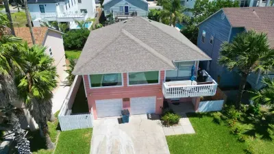 Charming coastal home with vibrant exterior, spacious balcony, palm‑lined yard, and easy beachside access—an inviting retreat in a relaxed island neighborhood.