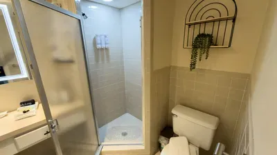 Bright, well‑kept bathroom featuring a glass‑door shower, fresh towels, warm neutral tilework, and a stylish wall accent with greenery—creating a clean, inviting space designed for comfort and ease during your stay.