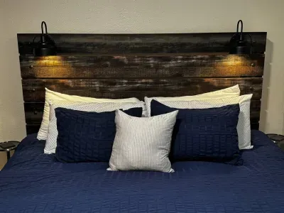 King bed with soft blue comforter, accent pillows, and a rustic wooden headboard with attached lights.