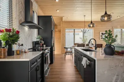 This modern kitchen is bright, functional, and open to the main living room. It features a large table with seating for eight—perfect for gathering, cooking, and connecting in a warm, welcoming space. Dishwasher, refrigerator, & oven pictured.