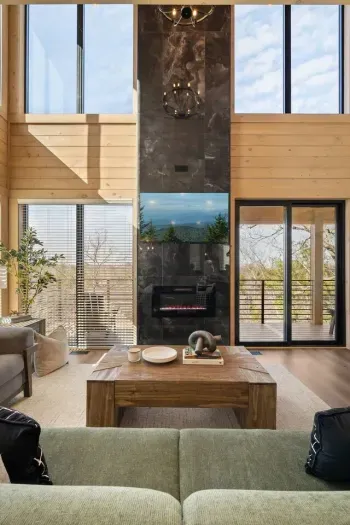 This space features a tall electric fireplace that adds a cozy, modern touch. Floor-to-ceiling windows fill the room with natural light and open up to a large private balcony. Step outside to comfortable seating and a peaceful, secluded view.