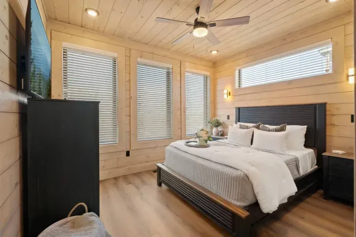 This bedroom includes a queen bed with an added foam topper for extra comfort, a wall-mounted TV for relaxing nights in, and convenient drawers for storing clothes or personal items—all wrapped in a cozy, stylish setting.
