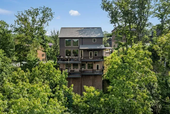 From the back, the cabin feels tucked into the Smokies — surrounded by lush green foliage that frames the balconies and makes the whole scene feel private and beautiful.