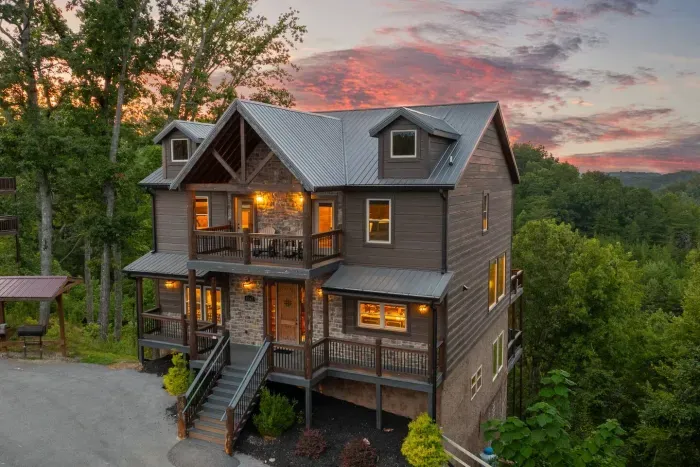 Front and center, the cabin stands with its open glass windows lit from within, glowing against the cotton candy mountain horizon. It’s the perfect balance of modern design and timeless Smoky Mountain vibes.