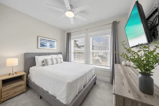 The queen bedroom keeps things simple, with a smart TV, a ceiling fan, and windows that catch the afternoon light.